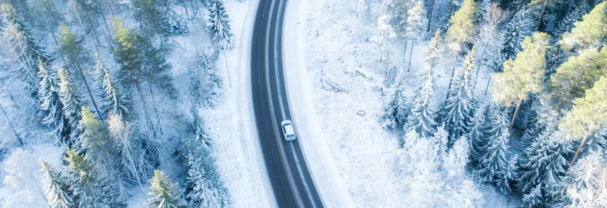 Voiture sur une route enneigée au milieu de la foret en hiver